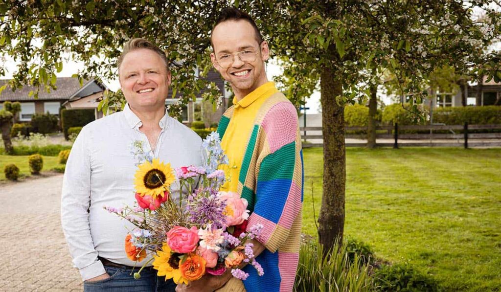 Twee mannelijke deelnemers van boeren bijbels en beauties staan op de foto met een boeket bloemen