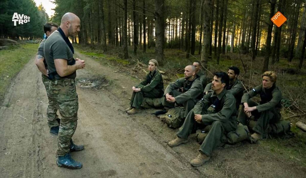 De Kamp van Koningsbrugge deelnemers zitten op de grond in het bos en luisteren naar instructeur Ray Klaassens en Dai Carter.