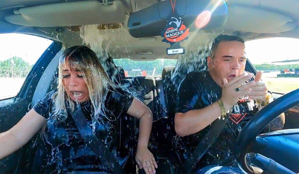 Deelnemers van De Slechtste Chauffeur van Nederland rijden in een auto terwijl er water over hun hoofd stroomt.