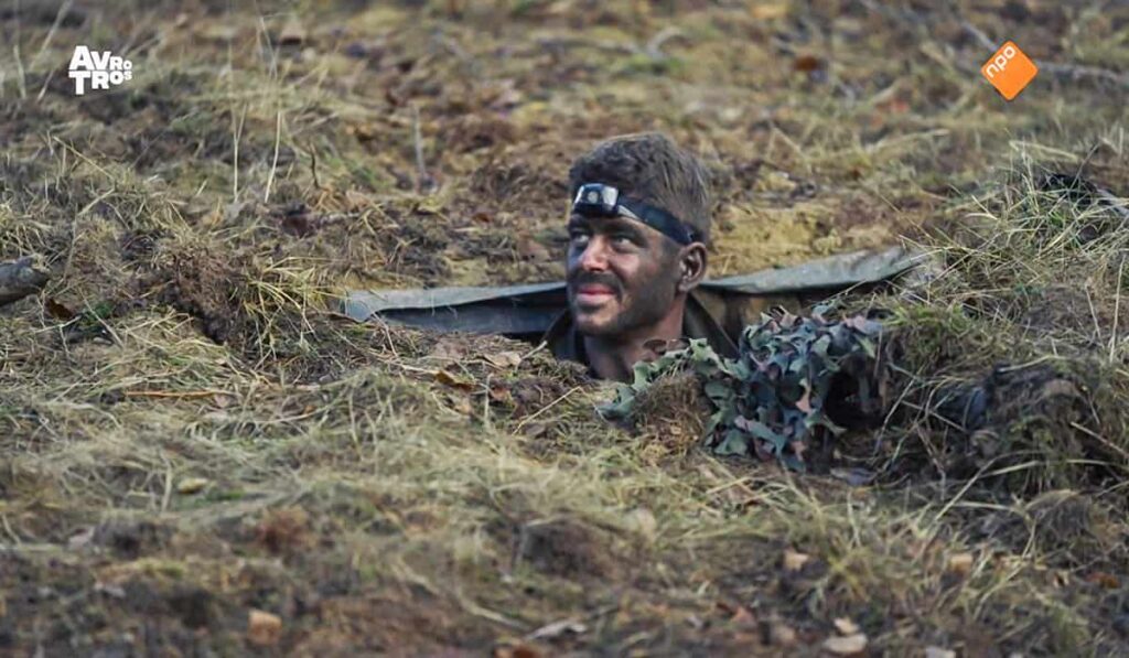 Remi van Empel, een van de deelnemers Kamp van Koningsbrugge 2023 steekt zijn hoofd uit een put in het gras tijdens de commando training.