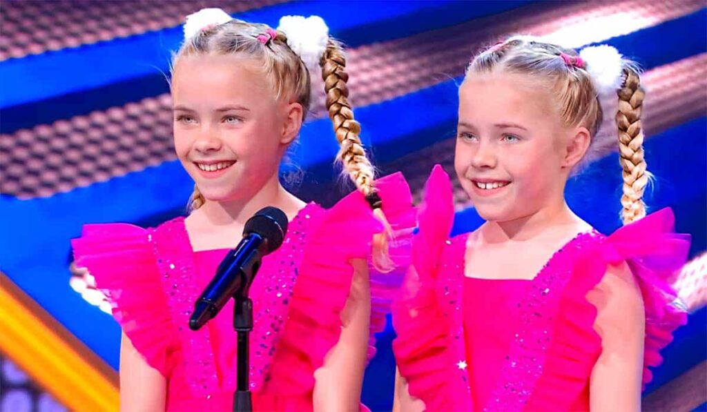 Tweeling Senna en Danae staan in roze jurkjes op het podium van Holland’s Got Talent 2023.