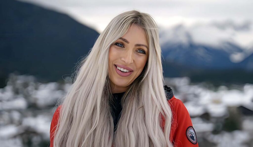 Blonde vrouw met lang haar (Denise uit Winter Vol Liefde) staat in rode jas voor besneeuwde bergen in Seefeld Oostenrijk.